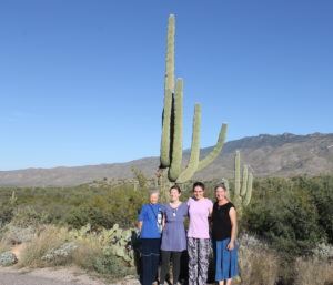 A group of four women standing in front of a large cactus in the desert