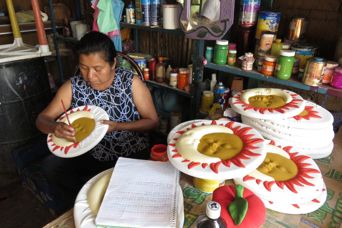 Photograph of a Mexican woman painting clay molds of the sun and moon.