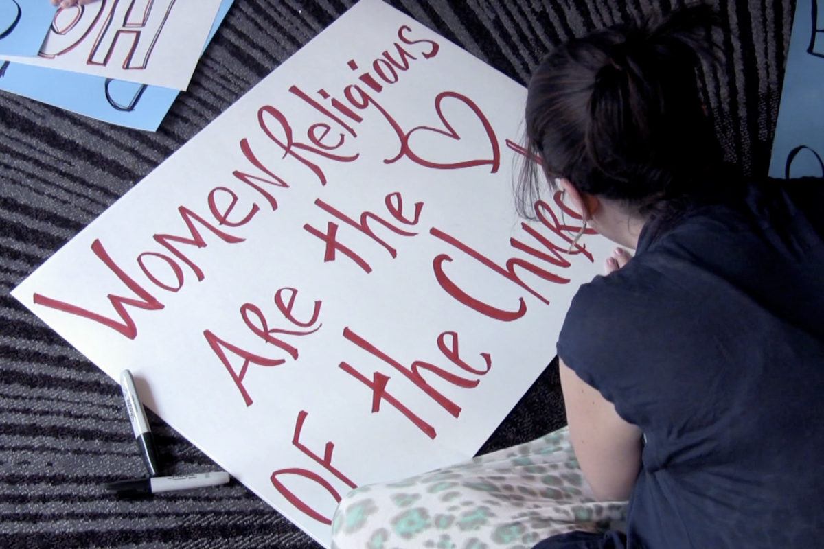 Photograph of a woman making a sign that reads "women religious are the heart of the church."