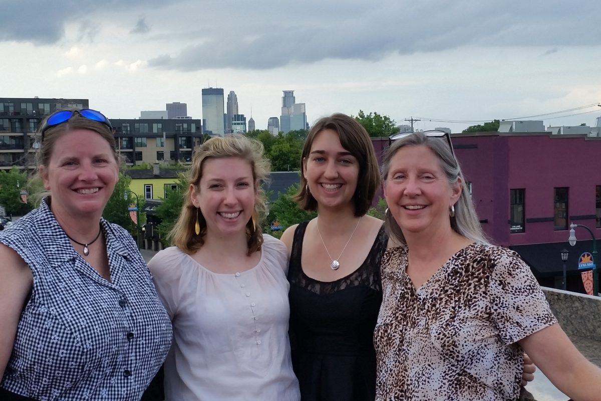 Photograph of four women on a rooftop with the Minneapolis skyline in the background.