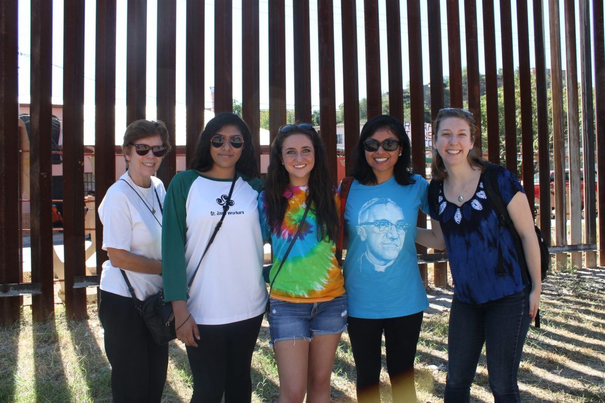 five young women in front of the US/Mexico border fence at the 2016 SOA Convergence at the Border