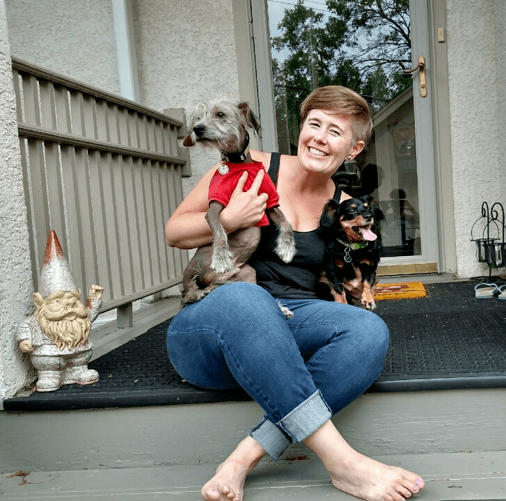 Robyn sitting on her front porch casually, smiling and holding her two small dogs.