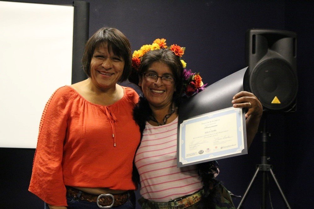 Photo of two women embracing, holding up a certificate of achievment.