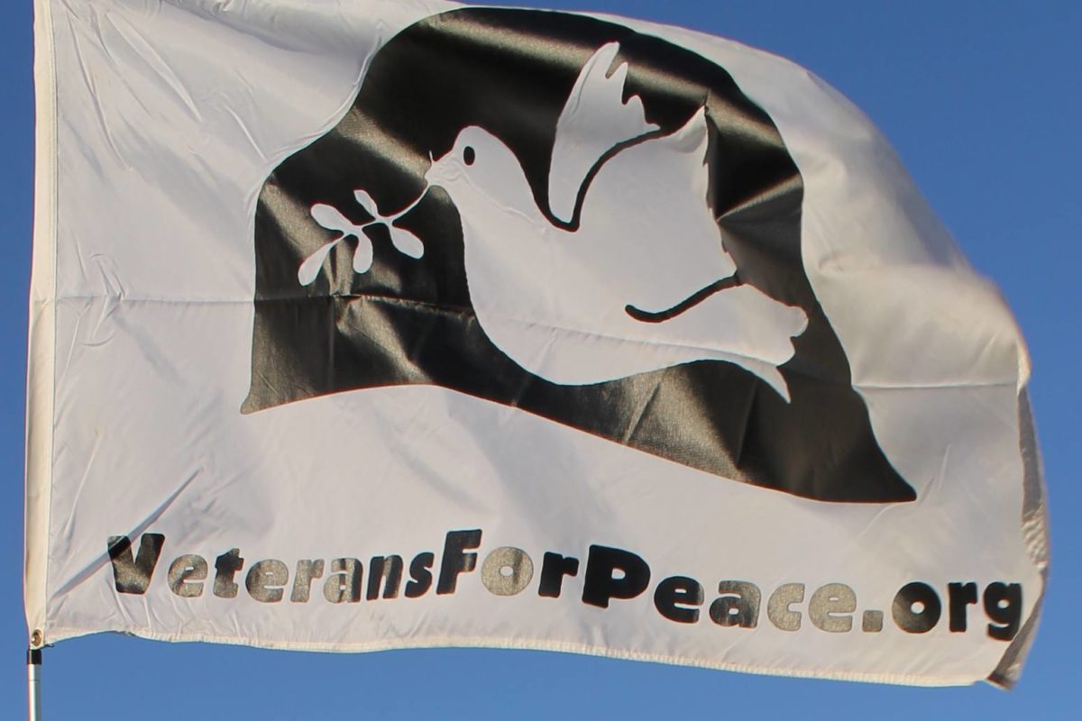 White flag with black helmet with a dove on it and the words veteransforpeace.org