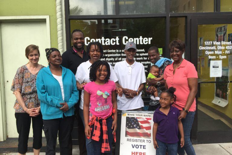 Group of adults and children standing outside of a building that says "Contact Center" on the door.