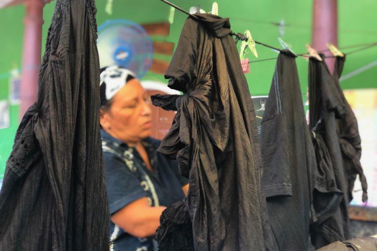 Photograph of a woman hanging indigo dyed fabric on a clothesline to dry.