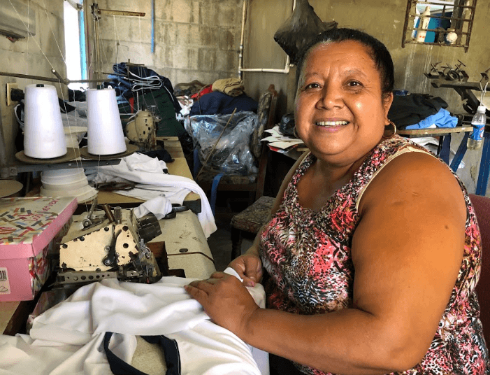 Photo of woman sitting at sewing machine showing her seamstress shop in El Salvador.